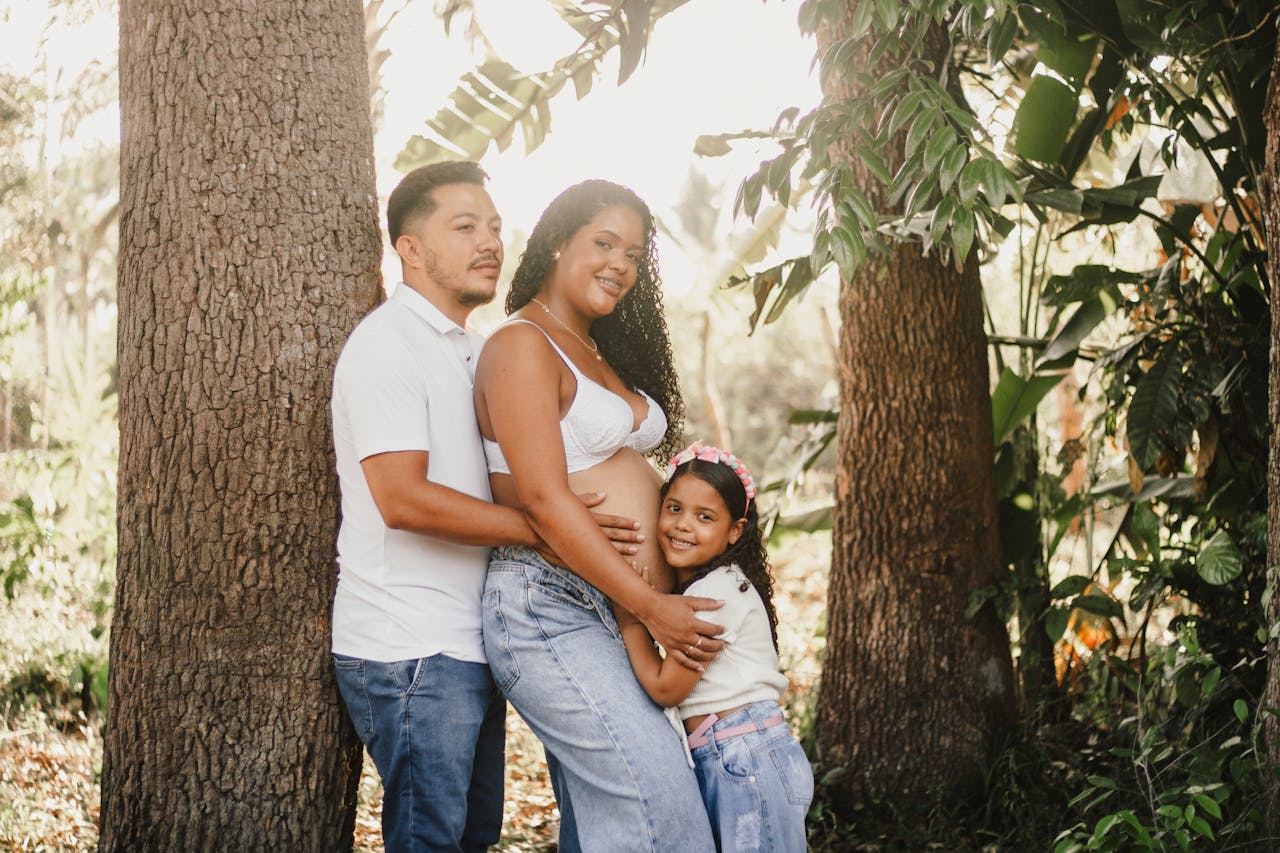 Happy family with pregnant mother outdoors in a sunny forest setting.