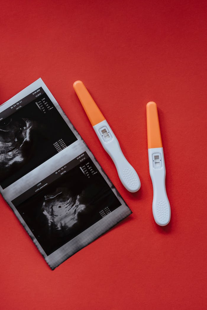 Two positive pregnancy tests and an ultrasound image placed on a red surface, indicating pregnancy confirmation.