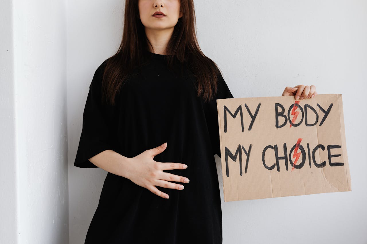 Woman holding 'My Body My Choice' sign, advocating for women's rights indoors.